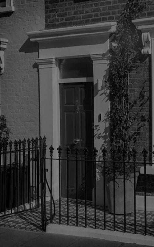 Front entrance of a classic London townhouse with a black door, iron fence, and brick facade.