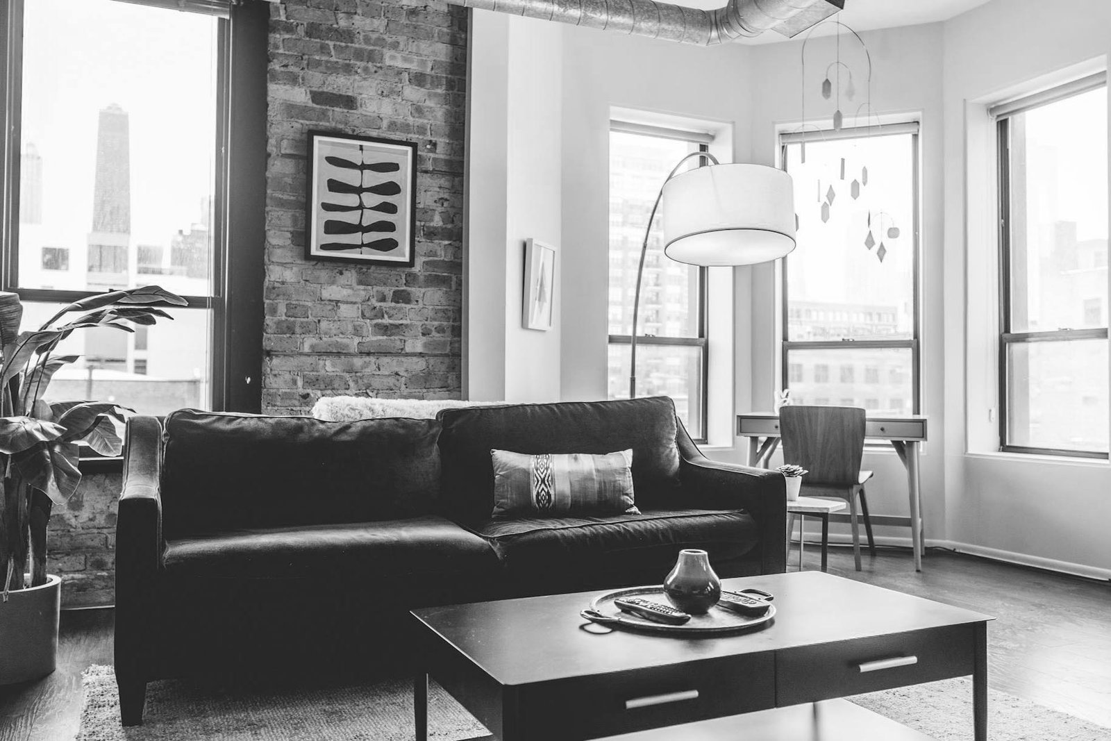 pexels-chaitaastic-1918291 Modern living room with exposed brick, large windows, a black sofa, and stylish decor.