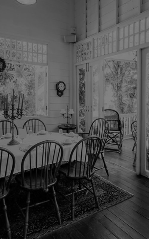 Cozy dining room with wooden chairs, a set table, and large windows overlooking a lush garden.